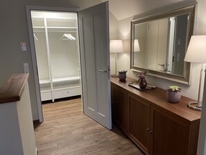 Ein begehbarer Kleiderschrank mit Kleiderstangen, ein Schminktisch mit Spiegel und eine Holzauslage mit zwei Lampen und einer Vase.