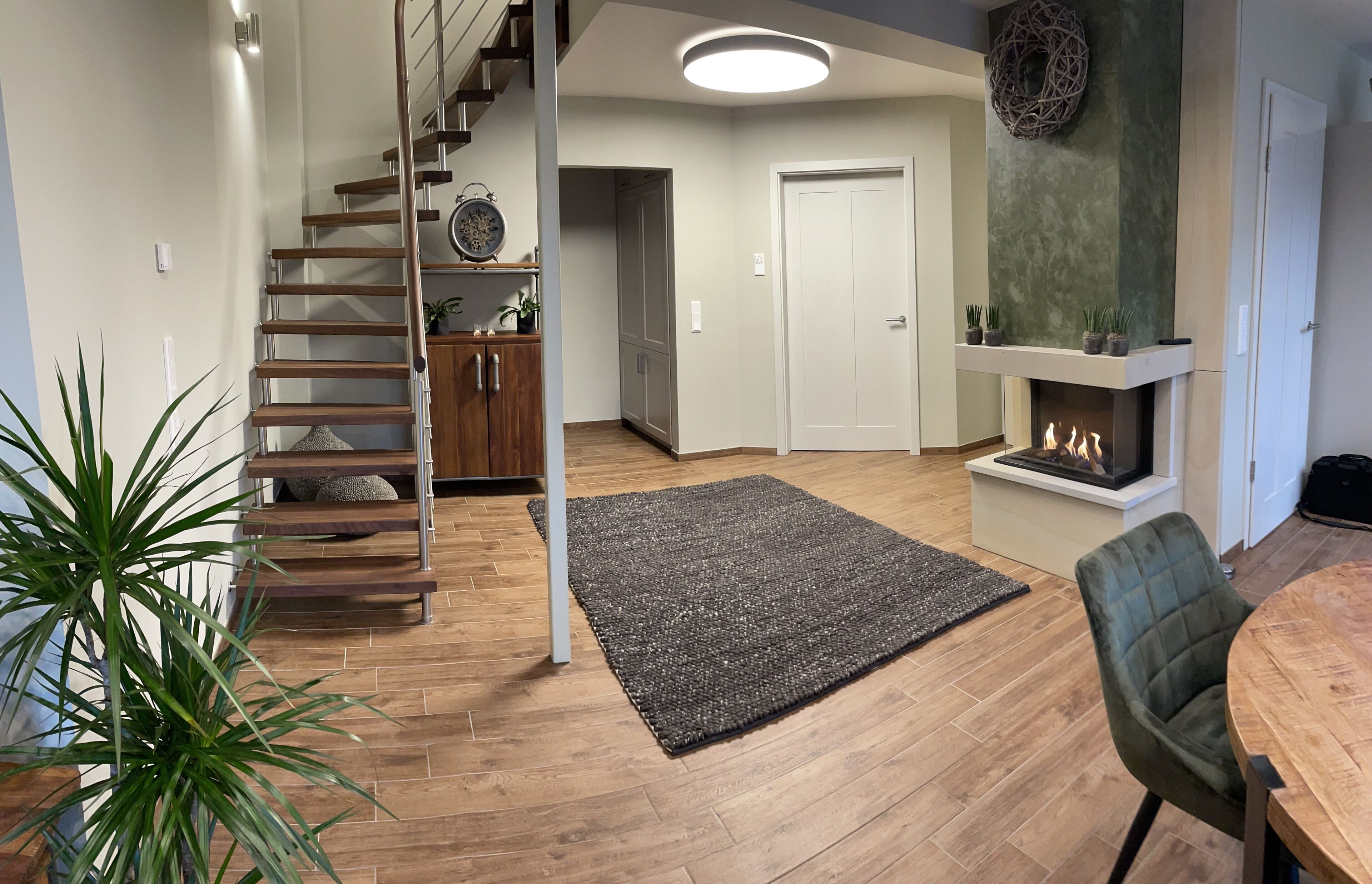 A modern living room with a wooden staircase, a fireplace, and a dining area with a table and chairs.