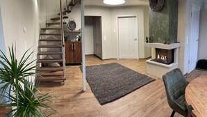 A modern living room with a wooden staircase, a fireplace, and a dining area with a table and chairs. - Exclusive maisonette vacation apartment (Coesfeld)