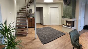 A modern living room with a wooden staircase, a fireplace, and a dining area with a table and chairs.