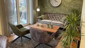 A modern living room with a grey sofa, a wooden coffee table with decorative items, a green armchair, and a large green plant. - Exclusive maisonette vacation apartment (Coesfeld)