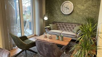 A modern living room with a grey sofa, a wooden coffee table with decorative items, a green armchair, and a large green plant.