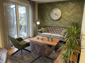 Ein modernes Wohnzimmer mit einem grauen Sofa, einem Holztisch mit Dekoration, einem grünen Sessel und einer großen Zimmerpflanze.