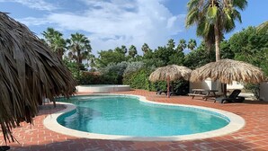 A swimming pool with a brick border, surrounded by palm trees and thatched umbrellas. - Caribbean Court Studio 321 with a refreshing shared pool and spectacular lagoon views (Kralendijk)
