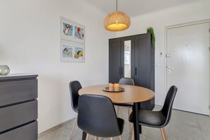 Un espace repas moderne avec une table ronde, des chaises noires, un luminaire en bois au plafond et des œuvres d’art accrochées au mur.