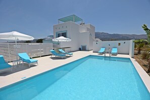 Un espace piscine avec des chaises bleues, des parasols et un b âtiment à la façade blanche et aux touches de couleur bleue.
