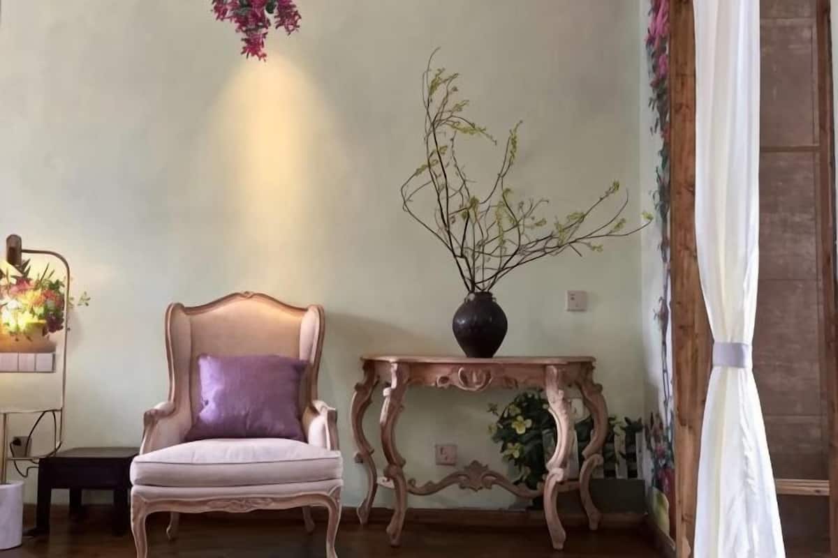 A room with a chair, a small table with a vase, and a wall with a floral painting.