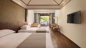 Une chambre d’hôtel avec deux lits, une télévision, un balcon avec une table et une vue sur la verdure.