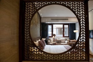 A hotel room with a large bed, a sitting area with a table and chairs, and a view through a decorative mirror. - Xiaoqi Lanyue Zuo'an Hotel (Wuyuan)