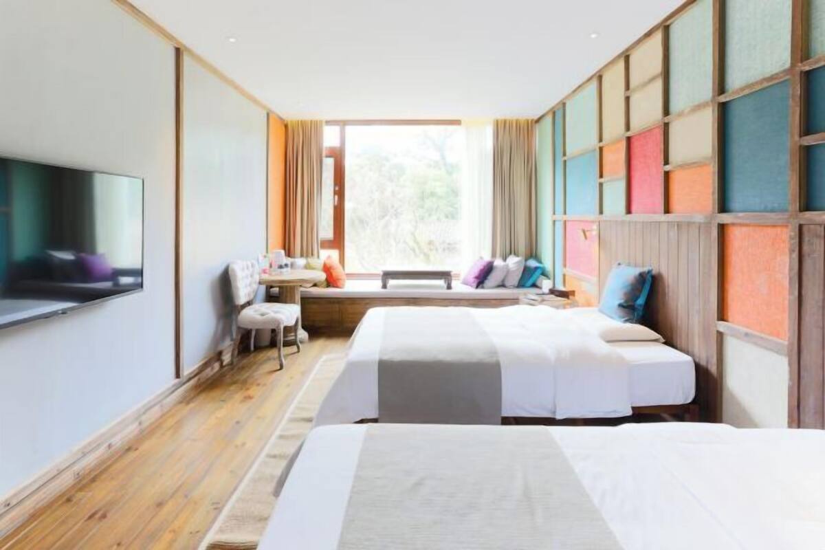 Habitación de hotel con dos camas, televisión, escritorio y ventana con cortinas.