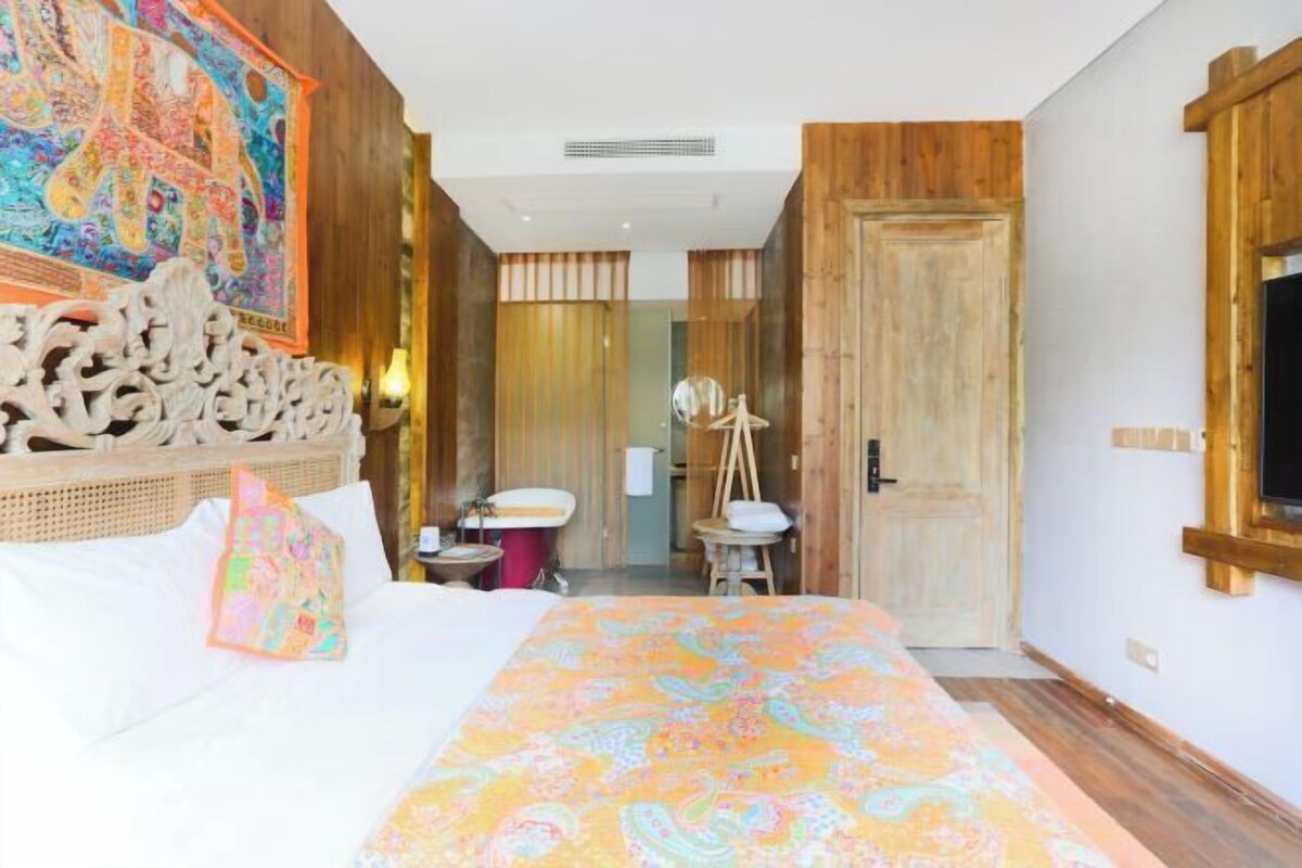Une chambre d’hôtel avec un lit, une salle de bain et un mur en bois orné d’une tapisserie colorée.