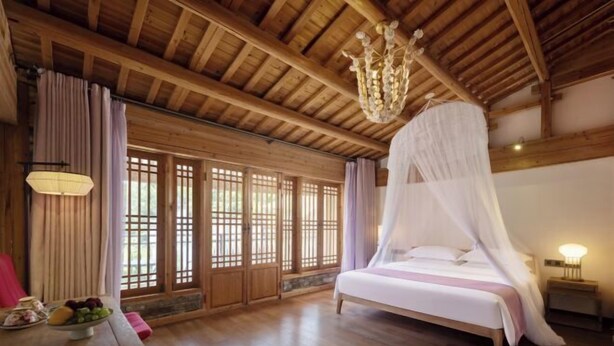 Une chambre avec un lit, un plafond en bois, de grandes fenêtres et un lustre.