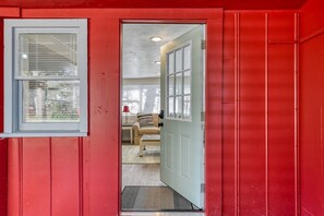 A red exterior with a white door and window, leading into a room with a beige sofa and a small table. - Little Palm Hideaway (St. Augustine)