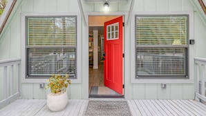 Una casa con puerta roja, dos ventanas con persianas, una planta en maceta y un felpudo.