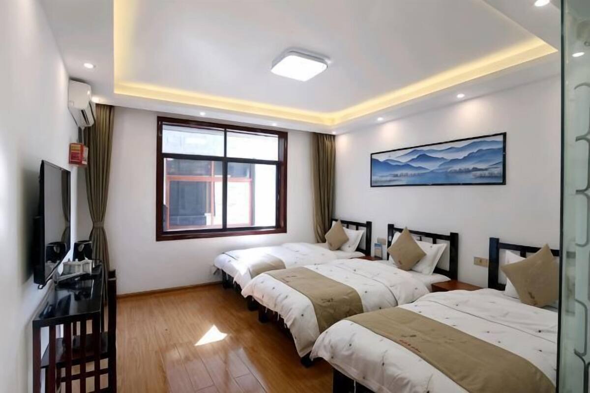 A hotel room with two beds, a TV, a window, and a painting on the wall.