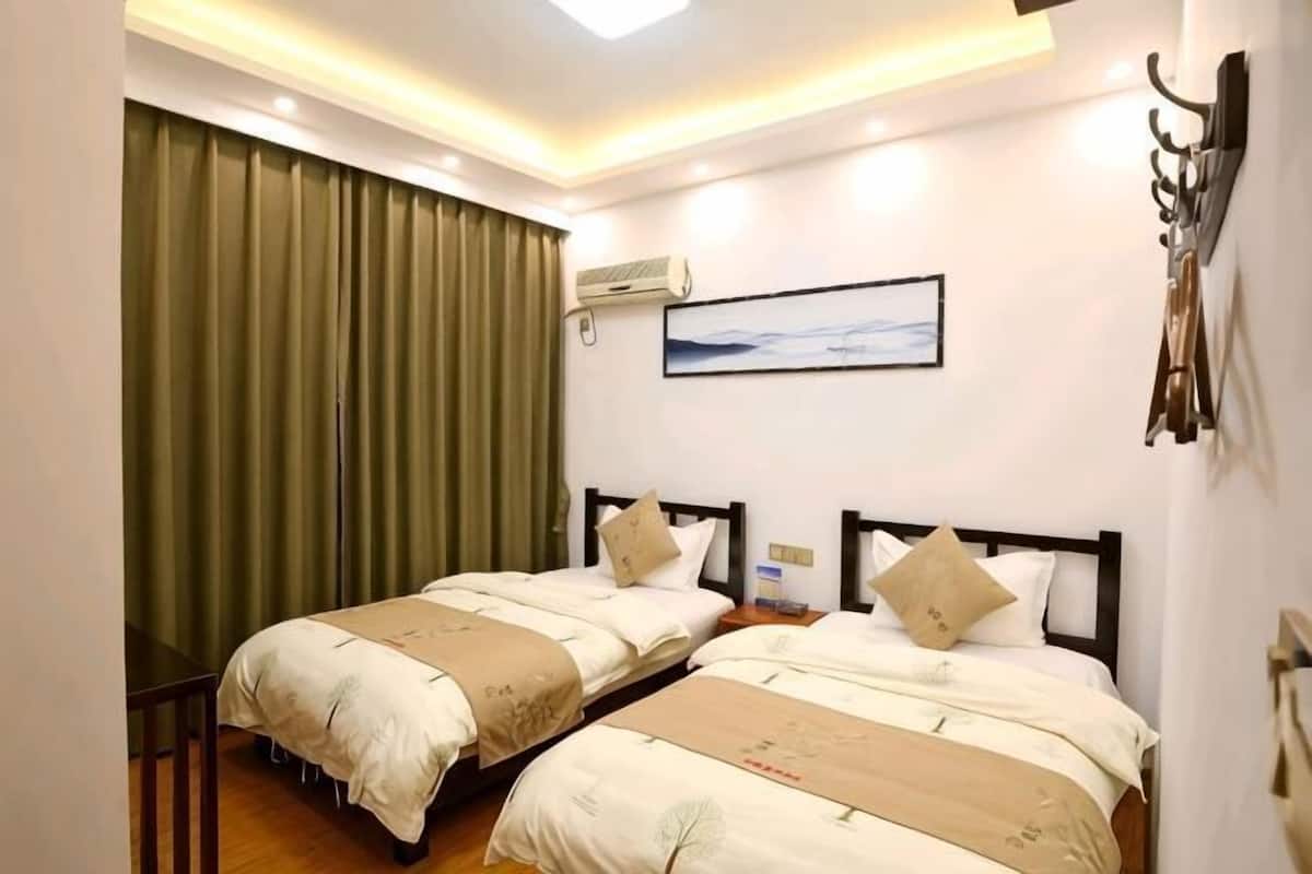 A hotel room with two beds, a large window with curtains, an air conditioning unit, and a painting on the wall.