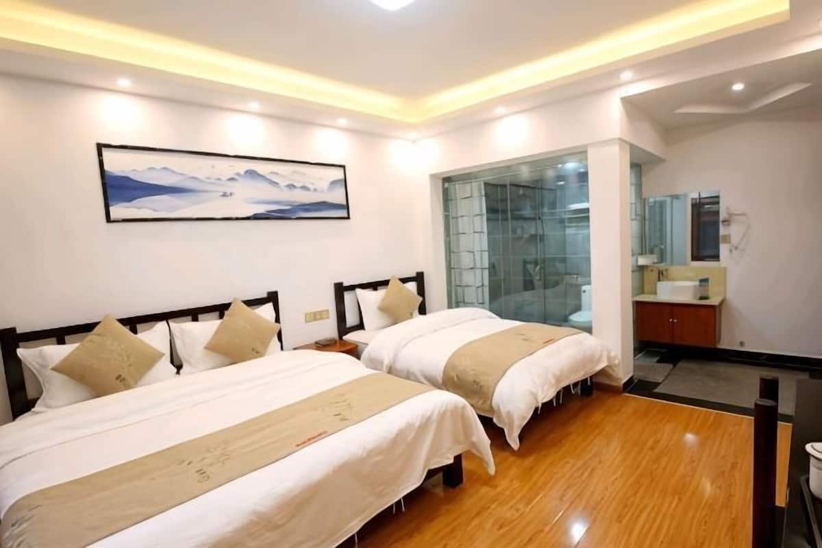 A hotel room with two beds, a large window, and a bathroom with a glass partition.