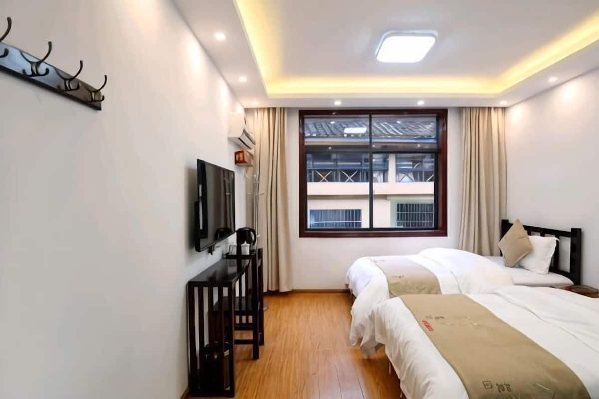 A hotel room with two beds, a TV, a desk, and a window with a view of buildings.