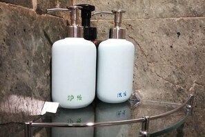 Due flaconi bianchi con dosatore su un ripiano in vetro, davanti a un muro in pietra.