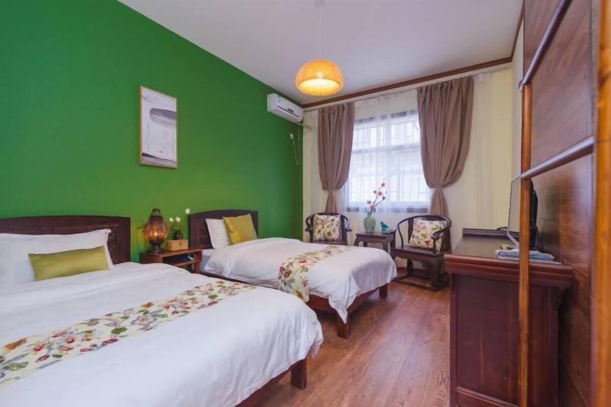 Hotellihuone, jossa on kaksi sänkyä, puinen lipasto, työpöytä ja ikkuna, jossa on verhot.