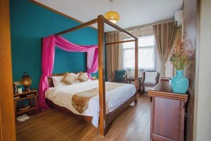Una cama con dosel adornada con cortinas rosadas, una mesita de noche de madera con lámpara, un aparador de madera y un jarrón con flores.