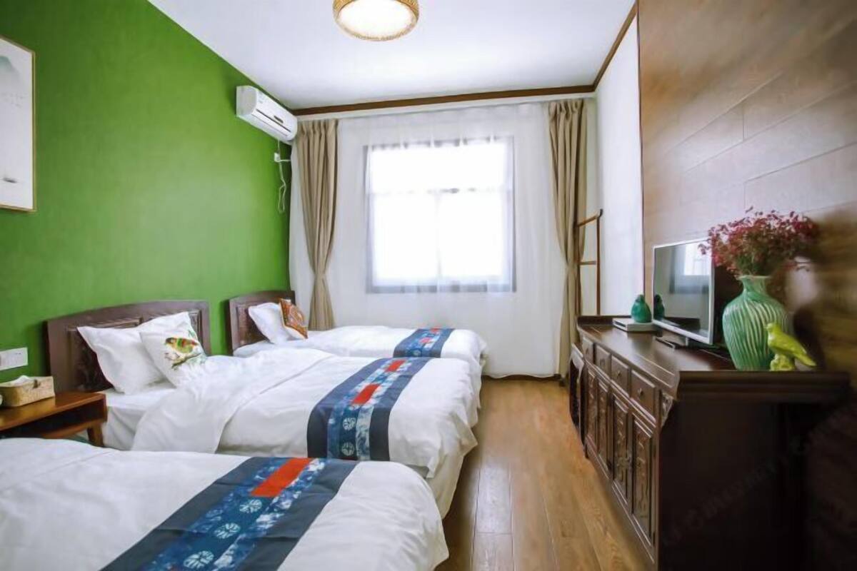 Hotellihuone, jossa on kaksi sänkyä, televisio, lipasto ja ikkuna, jossa on verhot.