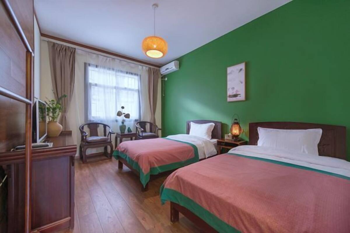 Hotellihuone, jossa on kaksi sänkyä, työpöytä, tuoli, ikkuna verhoilla ja vihreä seinä.