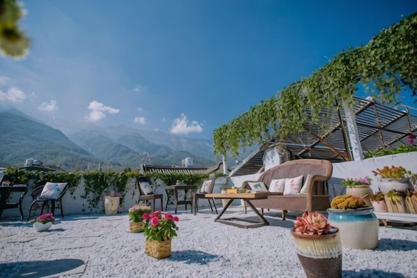 Una terraza con mobiliario exterior, un sofá de mimbre y plantas en macetas.