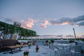 A rooftop terrace with outdoor seating, potted plants, and a view of the sky.