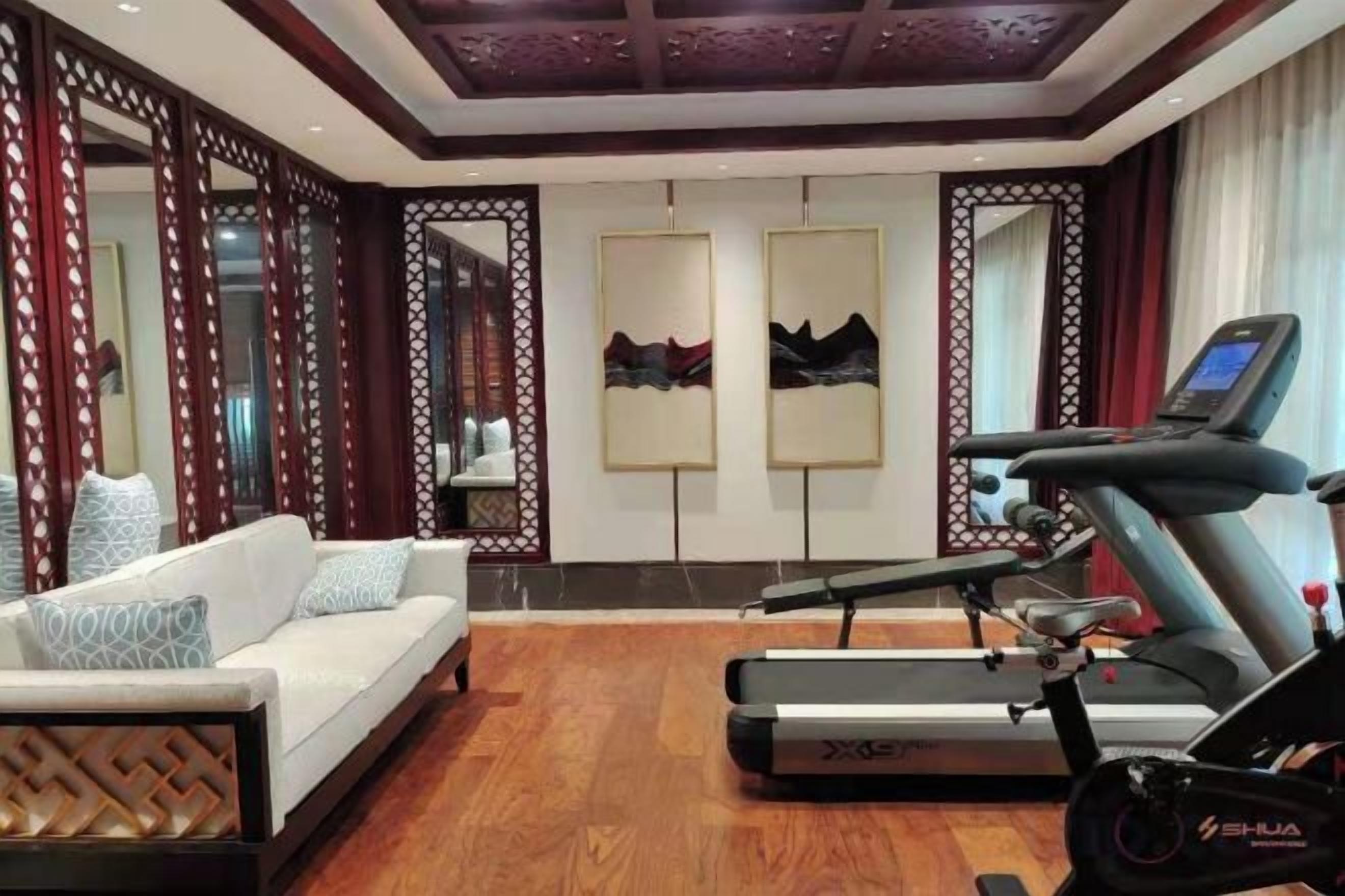 A room with a treadmill, a sofa, and a mirror.