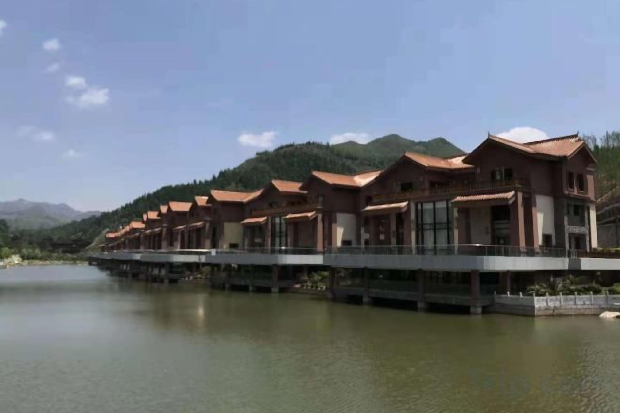 Une rangée de bâtiments de style traditionnel, avec un plan d’eau au premier plan et des montagnes en arrière-plan.