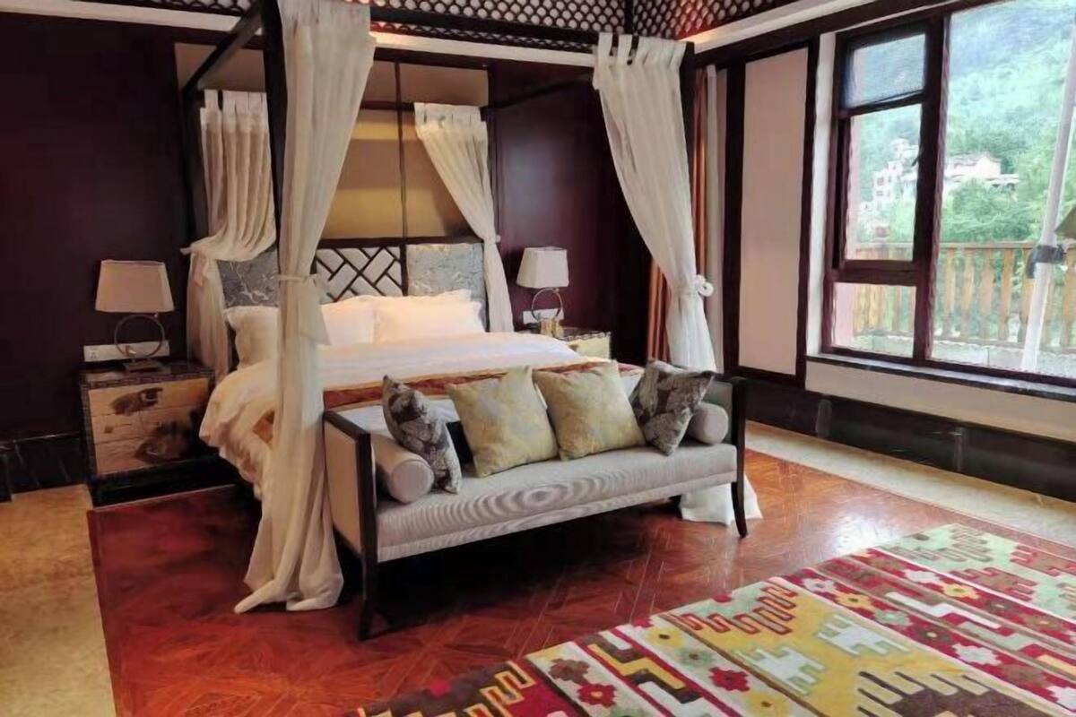 Una cama con dosel y cortinas blancas, un sofá con cojines y una alfombra estampada.