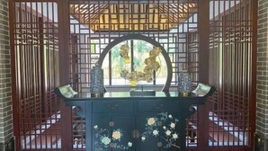 A traditional-style room with a dark wooden cabinet featuring floral designs, a circular window with a decorative metal frame, and a wooden lattice partition.