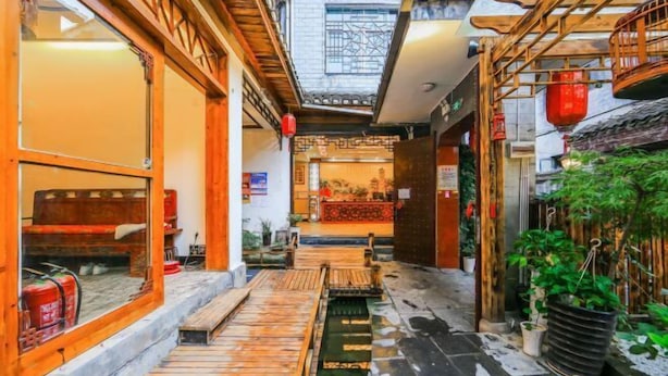 Un estrecho callejón con bancos de madera, una pequeña fuente de agua y plantas en macetas.