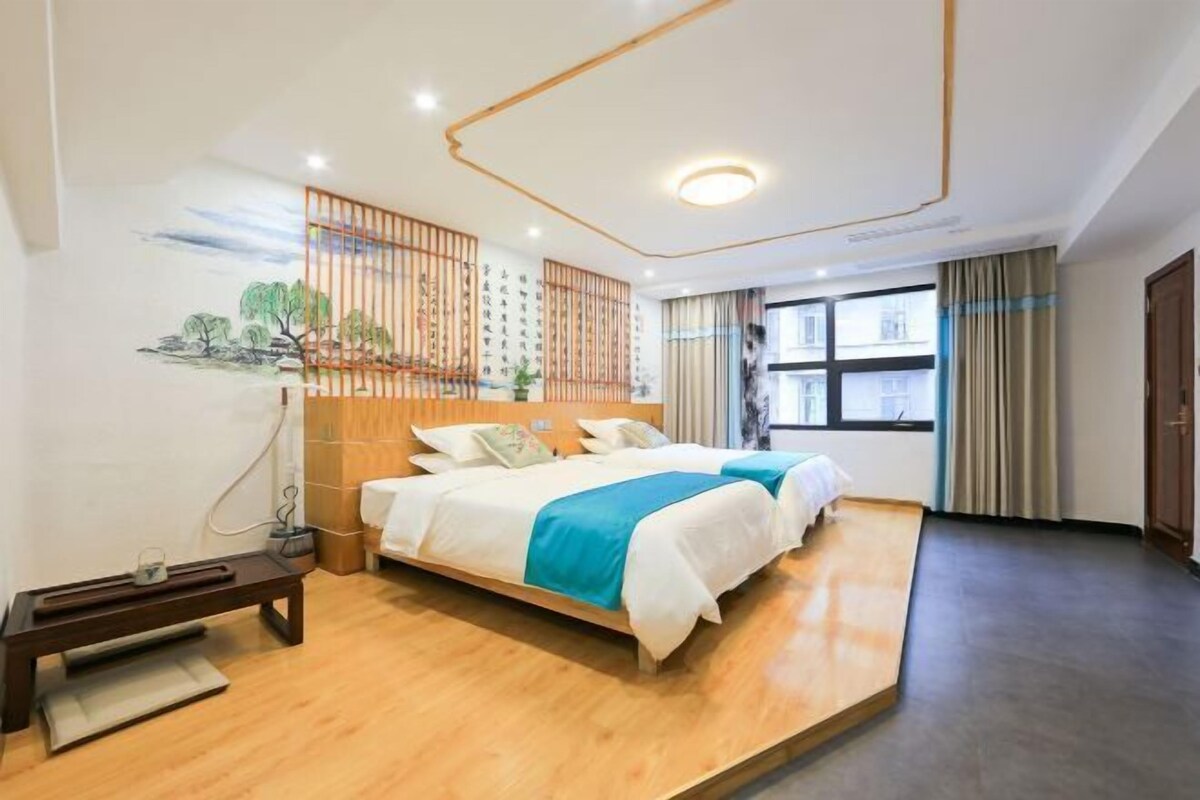 Ein Hotelzimmer mit Bett, Schreibtisch, Fenster und einer Wand mit Kunstwerken.