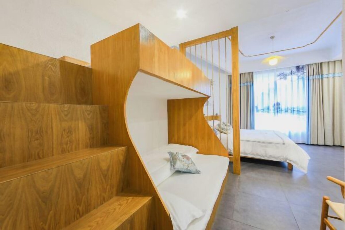 Ein modernes Hotelzimmer mit einer Holztreppe, einem Bett, einer Bank und Blick ins Freie.