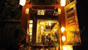 Una entrada tradicional al estilo japonés con un torii de madera, linternas y plantas en macetas.