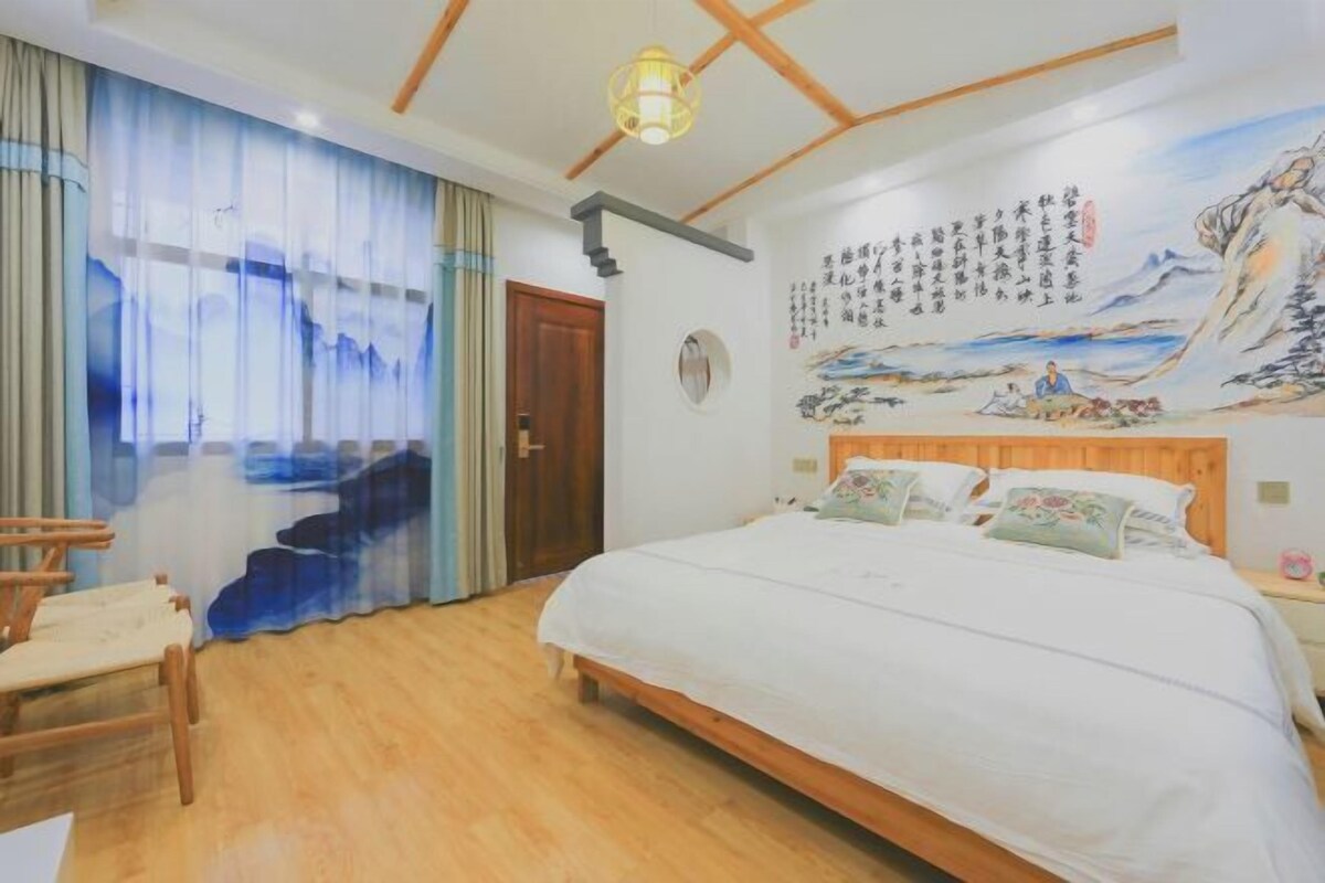 Ein Schlafzimmer mit einem hölzernen Bett, einem Sessel, einem großen Fenster mit Vorhängen und einem Wandbild.