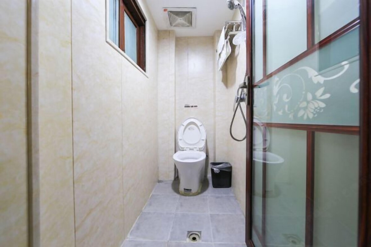 Ein schmales Badezimmer mit Toilette, Dusche und einem kleinen Mülleimer.