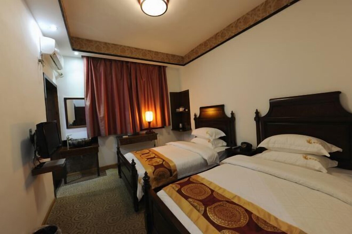 Ein Hotelzimmer mit zwei Betten, einem Schreibtisch, einem Stuhl, einem Fernseher und einem fenster mit Vorhängen.