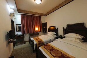 Ein Hotelzimmer mit zwei Betten, einem Schreibtisch, einem Stuhl, einem Fernseher und einem fenster mit Vorhängen.