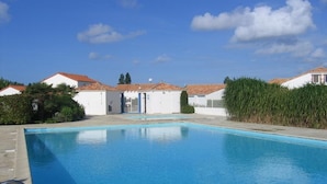 A swimming pool with a clear blue water surface, surrounded by white buildings with red-tiled roofs. - Vendean house with private pool, near beach, 5 people (La Faute-sur-Mer)