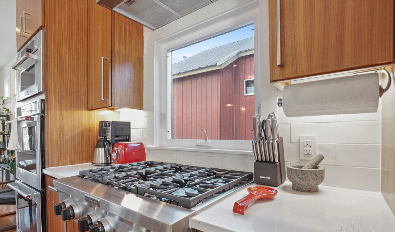A modern kitchen with wooden cabinets, stainless steel appliances, a gas stove, and a red kettle.