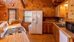 A cabin-style kitchen with wooden walls, a gas stove, a refrigerator, a sink, and a microwave. - Compton Mountain Cabin w/ Big Mountain Views (Ponca)