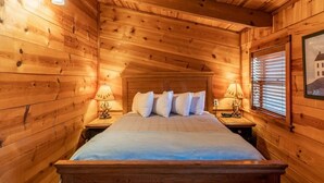 A wooden cabin bedroom with a bed, two bedside lamps, and a framed picture on the wall. - Compton Mountain Cabin w/ Big Mountain Views (Ponca)