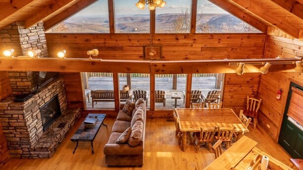 A spacious loft with a high ceiling, a stone fireplace, a sofa, a dining table, and multiple chairs. - Compton Mountain Cabin w/ Big Mountain Views (Ponca)