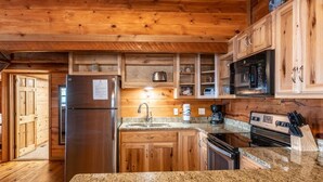 A kitchen with wooden cabinets, a stainless steel refrigerator, granite countertops, a microwave, and a stove. - Windridge Cabin w/ Beautiful View (Ponca)