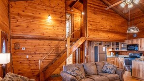 A wooden cabin interior with a sofa, a lamp, a ceiling fan, and a kitchen area. - Windridge Cabin w/ Beautiful View (Ponca)