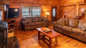 A wooden cabin interior with two sofas, a television, a fireplace, and a staircase. - Windridge Cabin w/ Beautiful View (Ponca)
