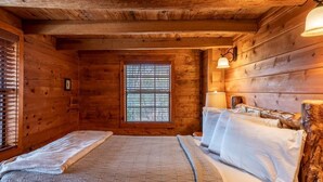 A wooden cabin room with a bed, a window with blinds, and a lamp. - Windridge Cabin w/ Beautiful View (Ponca)